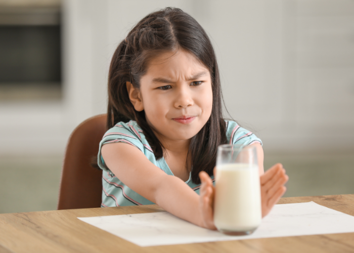 Kind schuift glas melk voor zich uit met een vies gezicht.