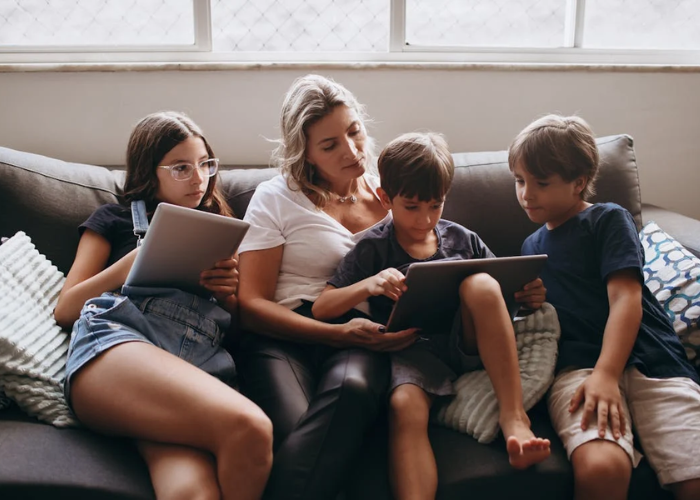 Moeder met 3 kinderen op de bank samen kijkend naar een tablet - behorend bij blog Schermtijd bij kinderen
