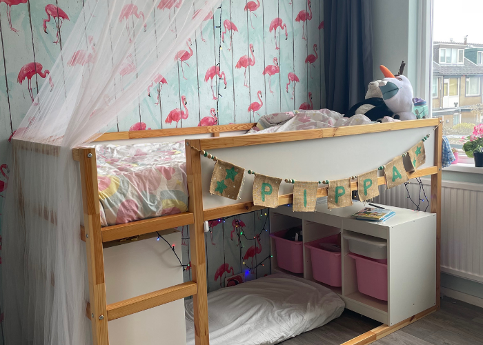 Je ziet een hoogslaper in een meisjeskamer met daaronder een gezellige lees- en speelplek.