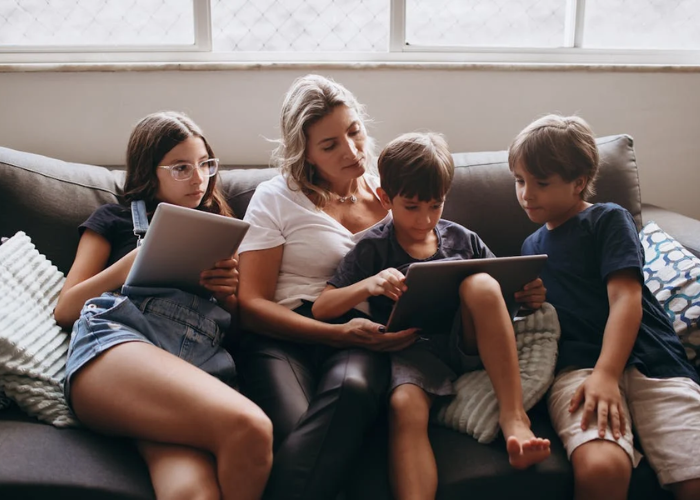 Moeder met 3 kinderen op de bank samen kijkend naar een tablet - behorend bij blog Schermtijd bij kinderen
